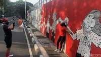 Warga berfoto di depan mural yang berisi pesan untuk bergandengan tangan melalui masa-masa sulit pandemi Covid-19, di Jl Tentara Pelajar, Jakarta, Selasa (1/2/2022). 