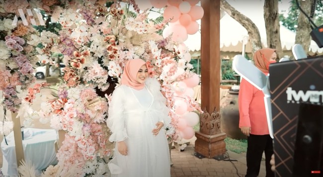 Aurel Hermansyah yang sebelumnya tidak tahu akan mendapatkan kejutan baby shower itu tampak berfoto terlebih dahulu sebelum memasuki lokasi inti acara. Aurel tampak cantik dalam balutan dress berwarna putih dan kerudung merah muda. Foto: YouTube/AH