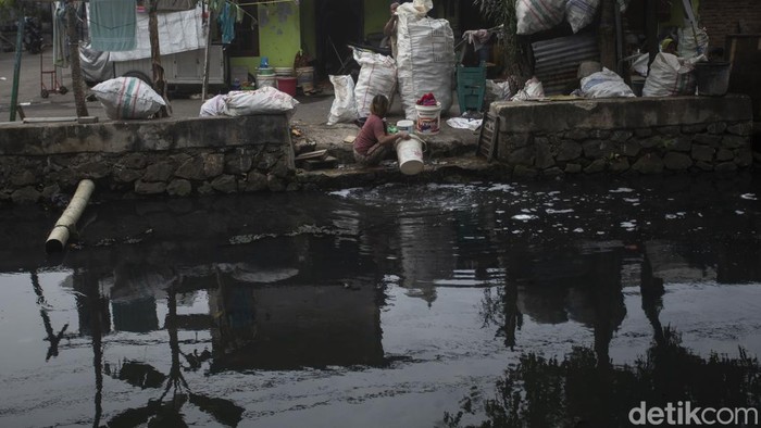 Seorang warga mencuci pakaian di kali Bambu Larangan, Cengkareng, Jakarta Barat, Rabu (2/2/2022). Kali berwarna hitam oekat ini masih digunakan oleh warga untuk mencuci pakaian, meski instalasi air bersih telah tersedia namun warga di sini tetap mencuci di kali.