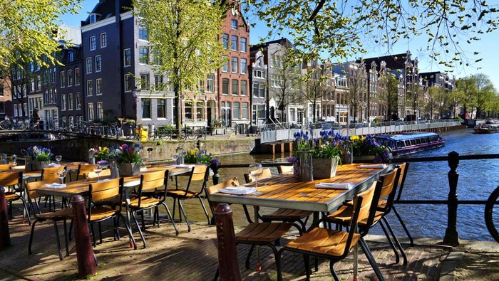 Restaurant tables lining the beautiful canals of Amsterdam under blue skies during springtime, Netherlands