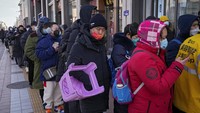 Seorang pria membawa kursi plastik saat ia dan ratusan penduduk berbaris untuk mengunjungi toko yang menjual memorabilia Olimpiade Musim Dingin 2022 di Beijing.