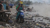 Pengendara roda dua melintasi tumpukan sampah yang terbawa ombak di Teluk Labuan, Pandeglang, Banten, Senin (7/2/2022).