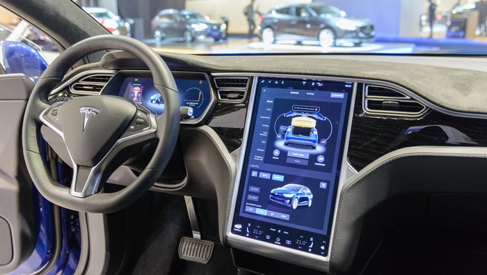 Brussels, Belgium - January 13, 2017: Luxurious interior on a Tesla Model X 90D full electric luxury crossover SUV car with a large touch screen and dashboard screen. The car is fitted with leather seats and aluminium details. The Model X uses falcon wing doors for access to the second and third row seats. The car is displayed on a motor show stand, with lights reflecting off of the body. There are people looking around and other cars on display in the background.