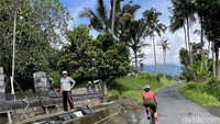 Pekerja melihat pesepeda melintas di jalanan pedesaan dengan latar pegunungan dan pesawahan luas di Bali, Desember 2021. Pekerja yang dibatasi oleh upah dan jam kerja sangat kontras dengan kebebasan pesepeda yang dapat menikmati waktu dan ruang sekuat kaki mengayuh.  (Ari Saputra/detikcom)