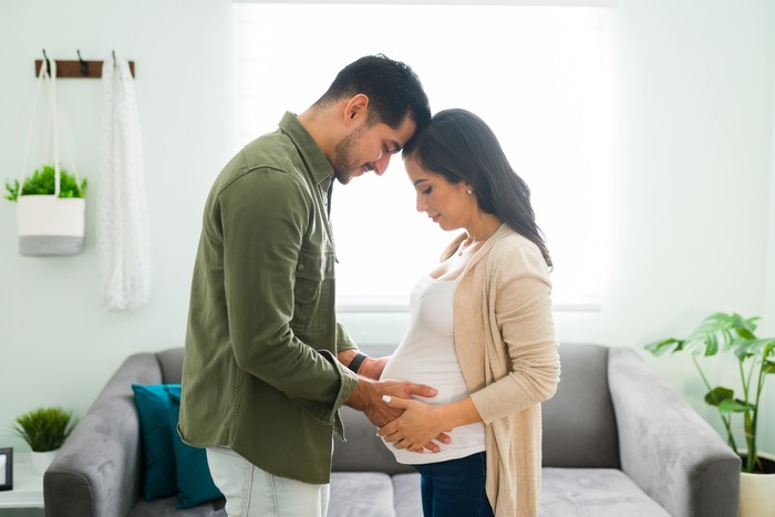suami istri Side view of a future mom and dad holding hands with their heads together. Beautiful beaming couple looking and gazing at the pregnant womans belly