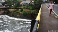 Warga melintas di Banjir Kanal Timur yang dipenuhi busa di Cipinang, Jakarta Timur, Senin (7/2/2022).