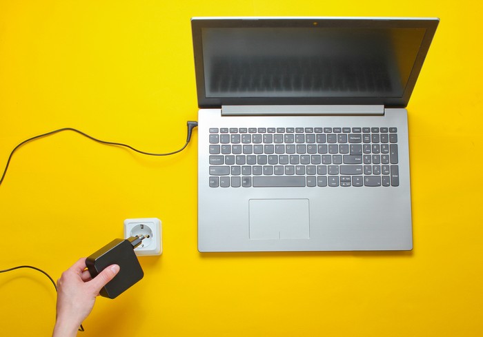 Laptop charger and electro outlet on a yellow background. The concept of electro addiction. Top view
