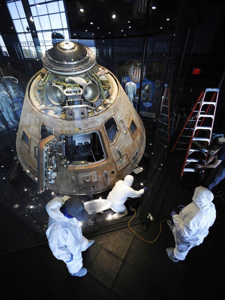 Workers open the glass case enclosing the Apollo 16 lunar capsule at the U.S. Space and Rocket Center in Huntsville, Ala., on Tuesday, Feb. 1, 2022. Following a break in routine maintenance because of the COVID-19 pandemic, the museum is sprucing up the antique spaceship before events marking the 50th anniversary of its flight to the moon in 1972. (AP Photo/Jay Reeves)