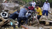 Sejumlah warga tampak bahu membahu mengangkat sebuah sepeda motor yang terdampak longsor. 
