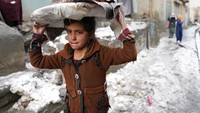 Anak kecil membawa roti di kepalanya melintasi jalan bersalju di Kabul, Afghanistan, Selasa, (8/2/2022). Kabul merupakan kota di pegunungan dengan ketinggian 1.700 mdpl. Pada musim dingin saat ini, cuaca turun hingga 1 derajat celcius.