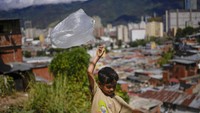 Anak kecil berusaha menerbangkan layang-layang dari kantong plastik, di San Agustin, Caracas, Venezuela, Sabtu, (29/1/2022). Siapa yang saat kecil sempat bermain ini, fix bahagia. (AP Photo/Matias Delacroix)