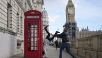 Turis asal Brazil bermain handstands di dekat telepon umum di London, Selasa (1/2/2022). Bertingkah konyol dan seperti anak kecil cukup memicu hormon bahagia. (AP Photo/Alastair Grant)