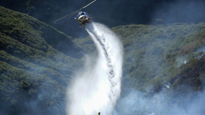Potret Petugas Berjibaku Padamkan Kebakaran Hutan di California Firefighters watch as a helicopter drops water on a wildfire in Laguna Beach, Calif., on Thursday, Feb. 10, 2022. A wildfire fanned by gusty Santa Ana winds erupted in hills on the Southern California coast early Thursday but firefighters kept flames from damaging homes and after several hours officials were optimistic the blaze could be stopped. (AP Photo/Ringo H.W. Chiu)