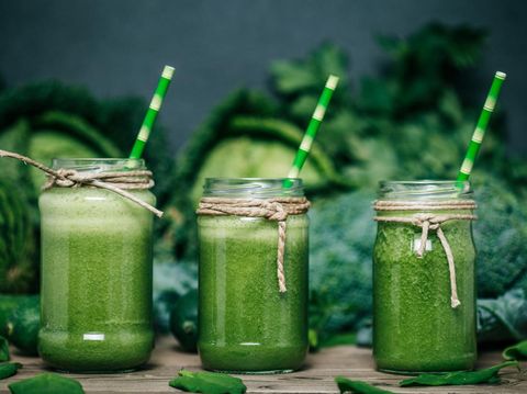 Blended green smoothie with ingredients on wooden table
