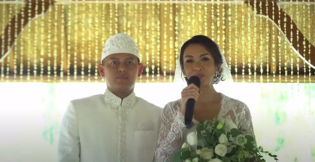 Keduanya memilih busana serba putih yang merupakan simbol kesucian dan kesakralan. Melanie tampak mengenakan kebaya lace putih lengkap dengan veil rancangan Anaz. Sementara Aldico berbusana beskap serta peci berwarna senada. Foto: YouTube Fit with MeL - by Melanie Putria