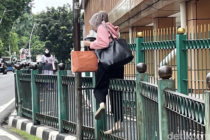 Sejumlah emak-emak yang merupakan penumpang KRL melakukan aksi nekat melompati pagar pembatas trotoar di Stasiun Cikini, Jakarta, Senin (14/02/2022).