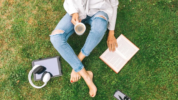Woman drinking coffee and sitting with book on the grass