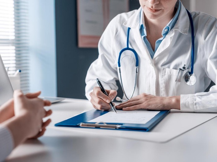 Doctor sitting at desk and writing a prescription for her patient