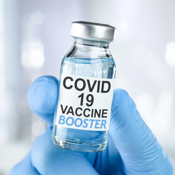 Hand in blue medical gloves holding a vaccine vial with Covid 19 Vaccine Booster text, for Coronavirus booster shot.