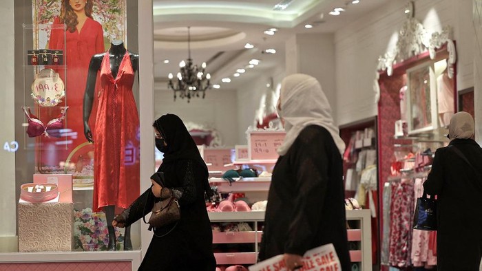 Perempuan Arab Saudi berjalan di depan etalase toko yang menjual baju dan pakaian dalam warna merah.