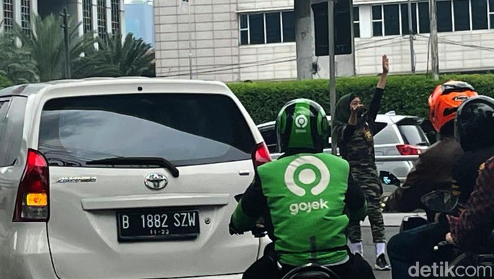 Seorang wanita berseragam loreng menjadi polisi cepek yang membantu mengatur lalu lintas di Jalan Gatot Subroto, Jakarta. Begini aksinya.