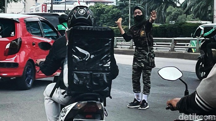 Seorang wanita berseragam loreng menjadi polisi cepek yang membantu mengatur lalu lintas di Jalan Gatot Subroto, Jakarta. Begini aksinya.