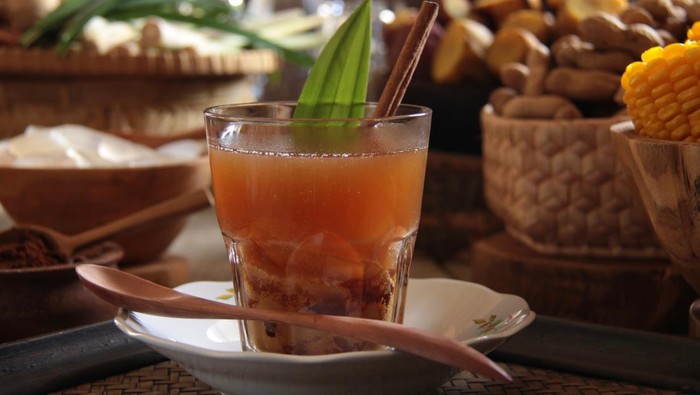 Bajigur, the traditional Sundanese hot herbal beverage of ginger tea, coffee, coconut milk and brown coconut sugar. In this variation, some palm fruit are added to the drink. The drink is garnished with pandanus leaf and cinnamon stick. It is arranged on a rustic wooden table together with typical steamed snacks that accompany this drink, such as steamed banana plantain, sweet potatoes, peanuts and corn on the cob.