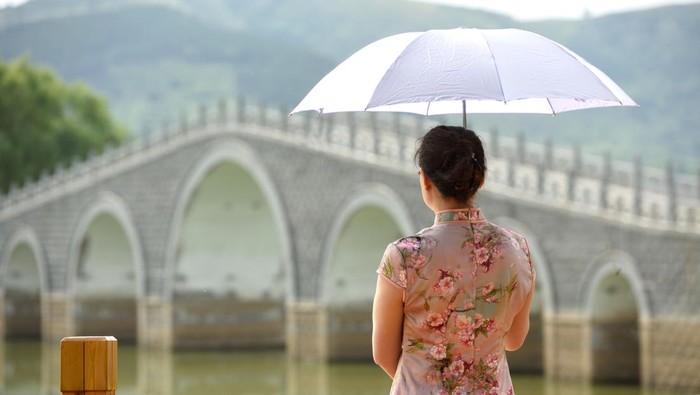 Women in traditional Chinese clothing walk in the landscape of ancient Chinese architecture.
