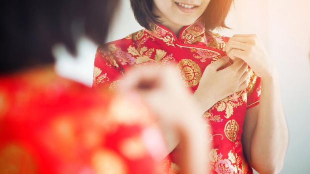 Chinese new year. Asian woman with cheongsam looking  to mirror. Girl is smiling. Get dress.