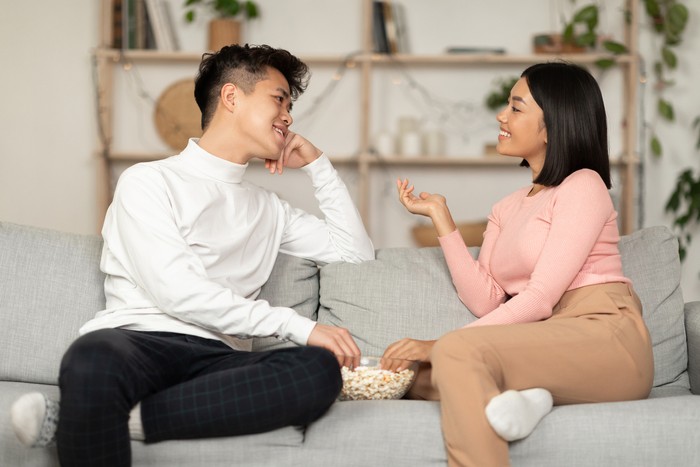 Korean Couple Flirting And Talking Enjoying Conversation During Stay-At-Home Date Spending Evening Together Sitting On Sofa Indoor. Romantic Relationship, Weekend Date Concept