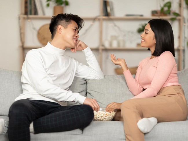Korean Couple Flirting And Talking Enjoying Conversation During Stay-At-Home Date Spending Evening Together Sitting On Sofa Indoor. Romantic Relationship, Weekend Date Concept