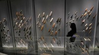 Seorang anggota staf berpose di samping berbagai kepala kapak batu yang dipamerkan di pameran The World of Stonehenge di British Museum di London.