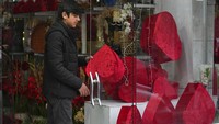 Seorang pria menghiasi jendela toko bunga dengan kotak merah berbentuk hati.