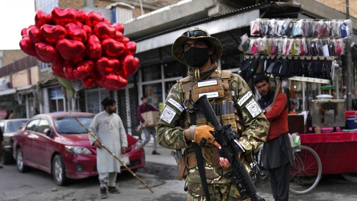 A Taliban fighter passes in front of a street vendor who sells red heart-shaped balloons for Valentine's Day in Kabul, Afghanistan, Monday, Feb. 14, 2022. Six months since Kabul was ceded to the Taliban with the sudden and secret departure of U.S.-backed president residents say a calm has settled on the country, but the future is uncertain as the economy teeters on the verge of an economic collapse and the new Taliban rulers tackle the transition from war to relative peace. (AP Photo/Hussein Malla)