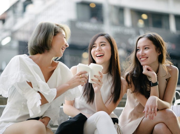 Young beautiful women shopping together, outdoors, smiling, using smartphone