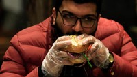Seorang pelanggan makan burger feseekh yang ditaburi daun emas dan dibuat dengan feseekh atau ikan asin.
