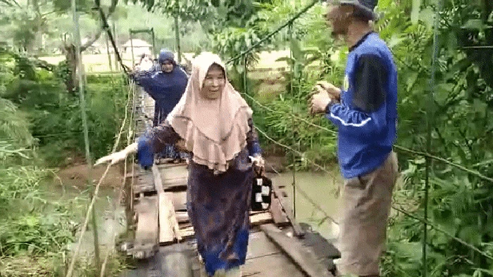 Warga melintasi jembatan gantung yang rusak di Sukabumi.