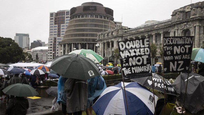 Protesters gather in wet conditions as they voice their opposition to coronavirus vaccine mandates at Parliament in Wellington, New Zealand, Saturday, Feb. 12, 2022. The protest began when a convoy of trucks and cars drove to Parliament from around the nation, inspired by protests in Canada. (George Heard/NZME via AP)