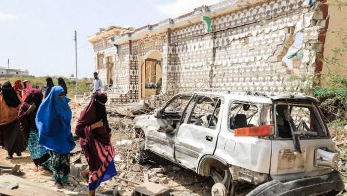 Women walk next to a destroyed house and the wreckage of a car following an explosion provocked by Al-Shabaab militants during an attacke to a police station on the outskirts of Mogadishu, Somalia, on February 16, 2022. - Al-Shabaab militants launched simultaneous attacks on police stations around Somalias capital Mogadishu overnight, killing two girls and wounding over a dozen people, security officials said Wednesday. (Photo by Hassan Ali Elmi / AFP)