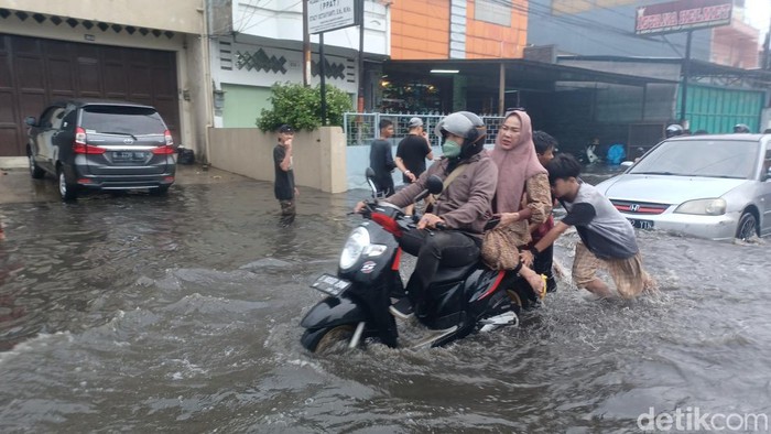 Banjir di Jalan Raya Kopo Sayati, Kabupaten Bandung membuat sejumlah masyarakat meraup keuntungan. Salah satunya adalah dengan membantu mendorong pengendara sepeda motor yang mogok, Sabtu, (19/2/2022).