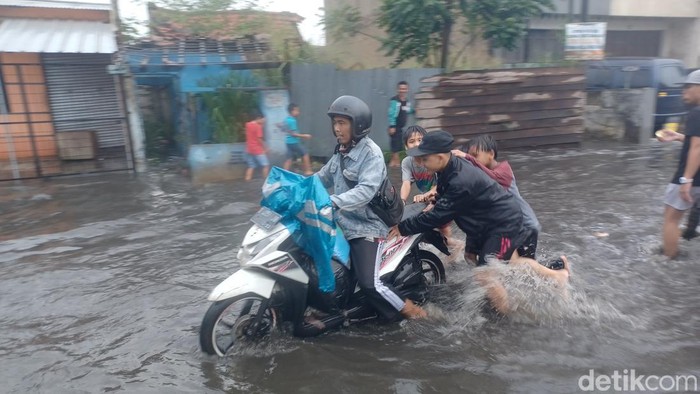 Banjir di Jalan Raya Kopo Sayati, Kabupaten Bandung membuat sejumlah masyarakat meraup keuntungan. Salah satunya adalah dengan membantu mendorong pengendara sepeda motor yang mogok, Sabtu, (19/2/2022).