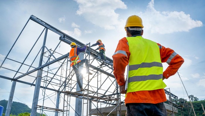 Engineer technician watching team of workers on high steel platform,Engineer technician Looking Up and Analyzing an Unfinished Construction Project.