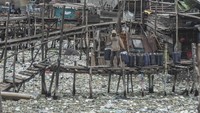 Warga memikul jeriken air melintasi jembatan kayu di antara sampah di kawasan perkampungan nelayan Cilincing, Jakarta, Minggu (20/2/2022). 