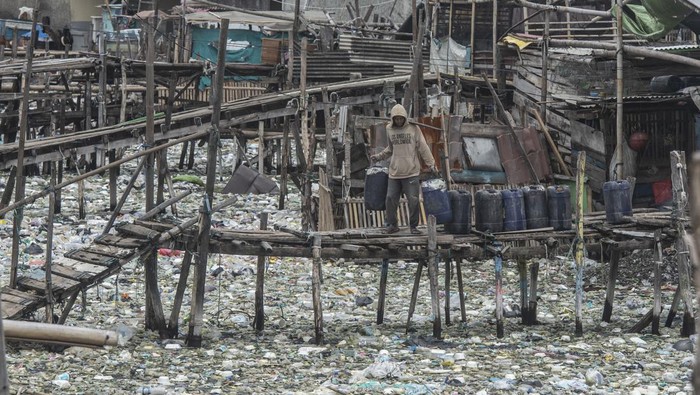 Perkampungan Nelayan Cilincing Dikepung Sampah Warga memikul jeriken air melintasi jembatan kayu di antara sampah di kawasan perkampungan nelayan Cilincing, Jakarta, Minggu (20/2/2022). Jelang peringatan Hari Peduli Sampah Nasional (HPSN) 2022, Pemprov DKI Jakarta mengajak warga Jakarta untuk peduli sampah mulai dari lingkungan terdekat minimal dengan cara memilah sampah dari rumah. ANTARA FOTO/Aprillio Akbar/tom.