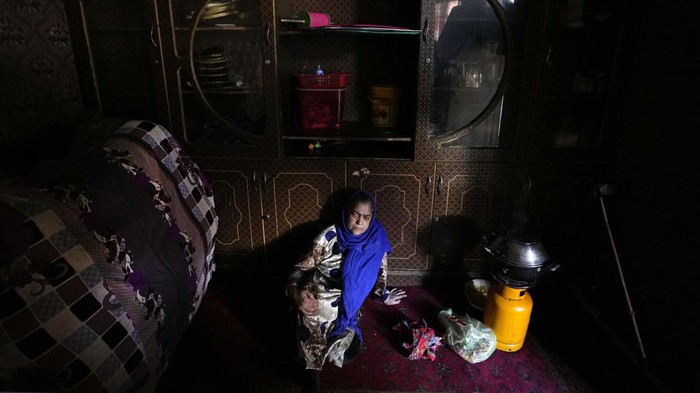 A woman sits on the ground as she cooks in her one room house, in Kabul, Afghanistan, Sunday, Feb. 20, 2022. (AP Photo/Hussein Malla)