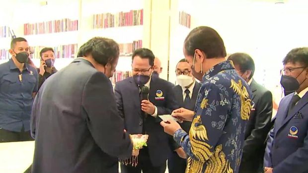 The moment President Jokowi received the Panglima Itam Library card from Surya Paloh.  The library card is for Jan Ethes and Sedah Mira, at NasDem Tower, Tuesday (22/2/2022).