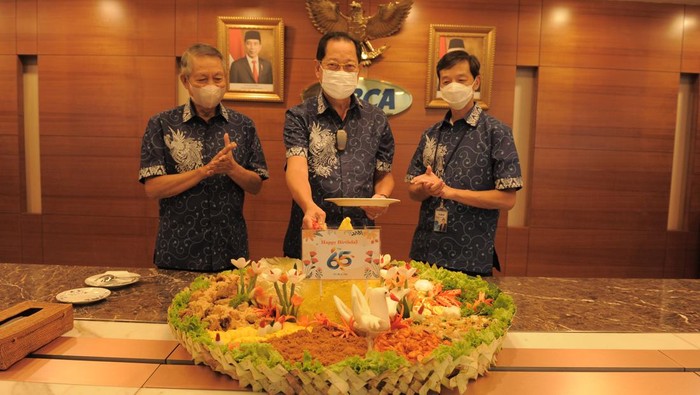 Presiden Direktur BCA Jahja Setiaatmadja (tengah) didampingi Wakil Presiden Direktur BCA Suwignyo Budiman (kiri) dan Wakil Presiden Direktur BCA Armand Wahyudi Hartono (kanan) secara simbolis memotong tumpeng di tengah acara perayaan HUT BCA ke-65 di Jakarta, Senin (21/02/2022).