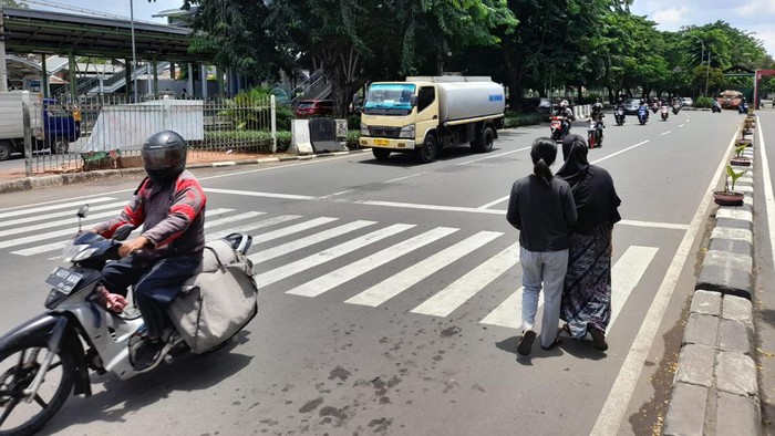 Warga menyeberang menuju akses masuk Stasiun Klender Baru, Jl I Gusti Ngurah Rai, Jakarta Timur. Mereka meminta pembuatan pelican crossing.