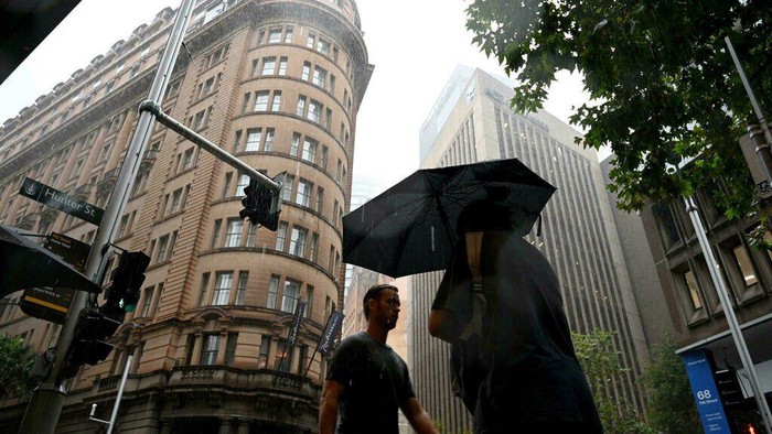 Pedestrians walk in heavy rain in the central business district of Sydney on February 22, 2022. (Saeed KHAN/AFP)