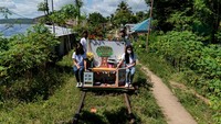Sebuah kereta lori kayu yang didekorasi dengan meriah di rel kereta api yang jarang digunakan di Filipina selatan membawa empat guru muda. Dua di depan dan dua di belakang mendorongnya dengan kaki mereka.